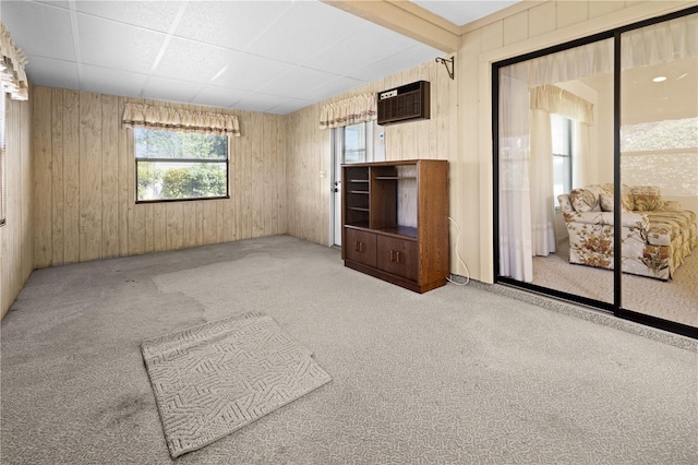 spare room featuring a wall mounted air conditioner, a drop ceiling, light colored carpet, and wood walls