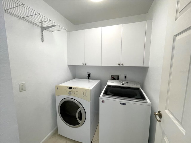 clothes washing area featuring cabinets, washing machine and dryer, and light tile patterned floors