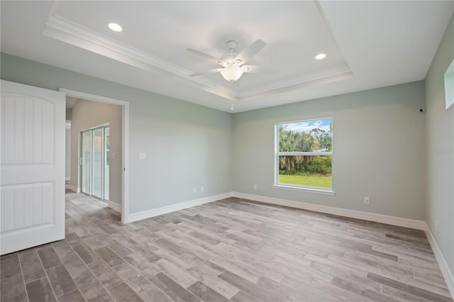 empty room featuring light hardwood / wood-style floors, ceiling fan, crown molding, and a raised ceiling