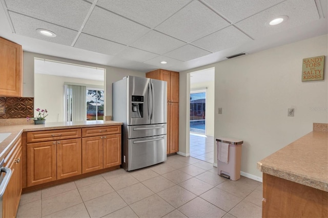 kitchen with stainless steel fridge with ice dispenser, a drop ceiling, backsplash, and light tile floors