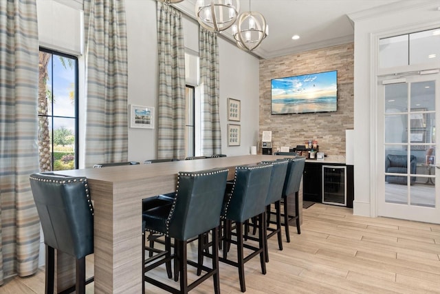 bar featuring crown molding, an inviting chandelier, light hardwood / wood-style flooring, wine cooler, and hanging light fixtures