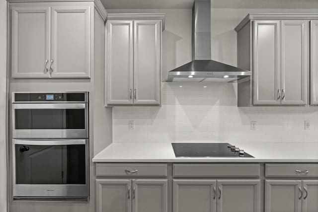 kitchen featuring tasteful backsplash, double oven, wall chimney exhaust hood, and black stovetop