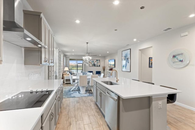 kitchen featuring black electric stovetop, wall chimney range hood, sink, a large island with sink, and dishwasher