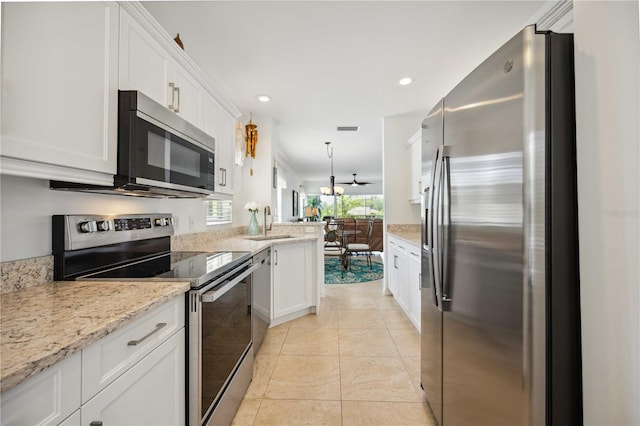 kitchen with hanging light fixtures, white cabinetry, appliances with stainless steel finishes, sink, and light stone counters