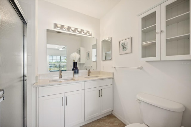 bathroom featuring a shower with shower door, vanity with extensive cabinet space, toilet, tile flooring, and dual sinks