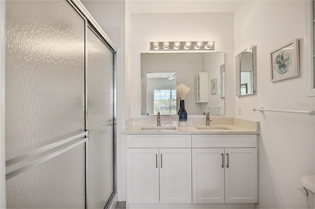 bathroom with a shower with shower door, vanity with extensive cabinet space, toilet, and double sink