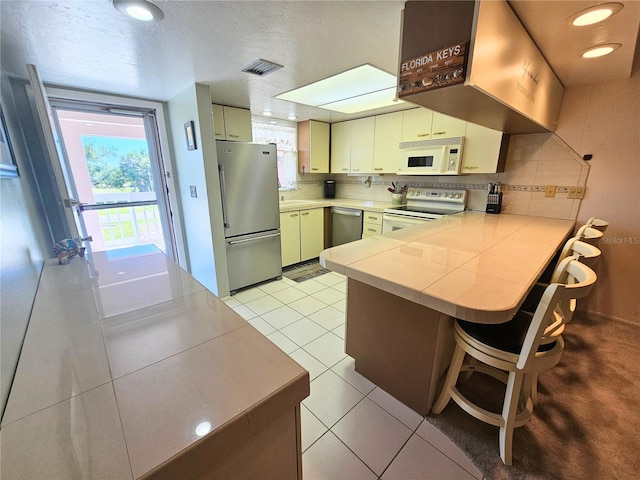 kitchen with stainless steel appliances, decorative backsplash, kitchen peninsula, light tile patterned flooring, and cream cabinetry