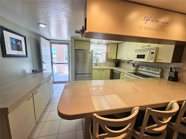 kitchen featuring tile countertops, kitchen peninsula, stainless steel appliances, a textured ceiling, and sink