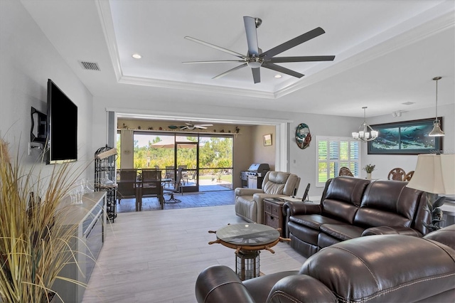 living room with ceiling fan with notable chandelier, a healthy amount of sunlight, light hardwood / wood-style flooring, and a raised ceiling