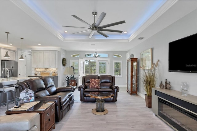 living room featuring ceiling fan with notable chandelier, light hardwood / wood-style flooring, a tray ceiling, and crown molding