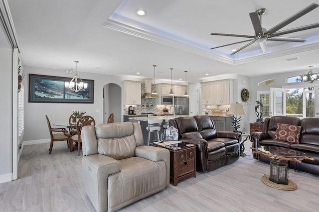 living room featuring ornamental molding, light hardwood / wood-style flooring, ceiling fan with notable chandelier, and a tray ceiling