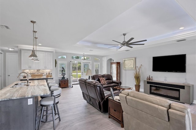 living room featuring light hardwood / wood-style flooring, a raised ceiling, ceiling fan, and sink