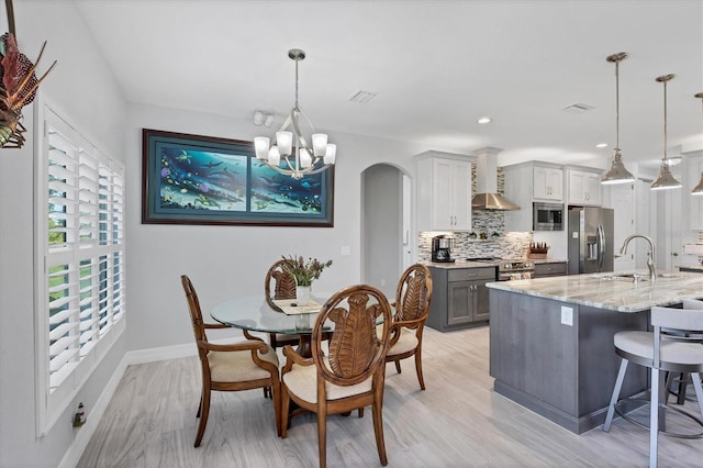 dining area with an inviting chandelier, sink, and light wood-type flooring