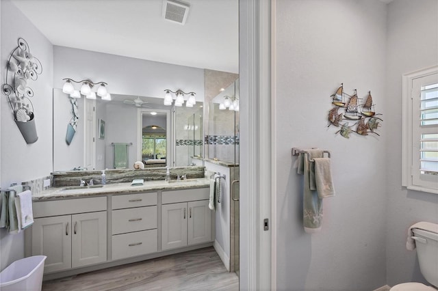 bathroom with vanity with extensive cabinet space, wood-type flooring, dual sinks, toilet, and ceiling fan