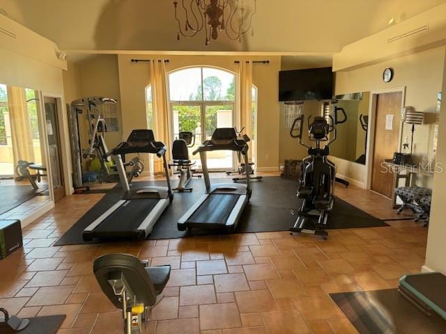 gym with tile patterned flooring, a high ceiling, and a chandelier