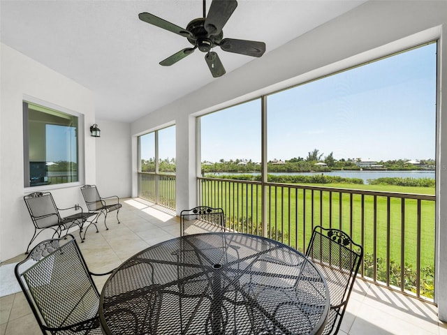 sunroom with ceiling fan and a water view