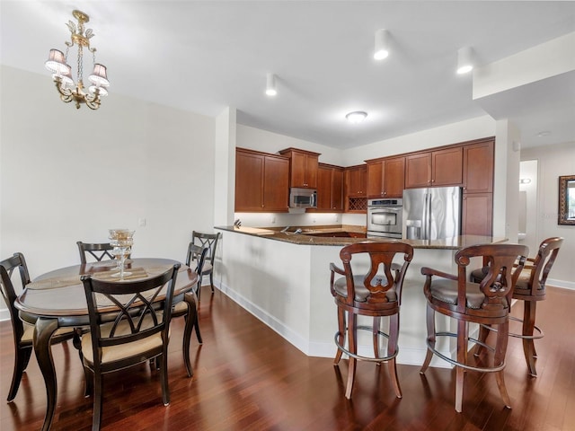 kitchen with stainless steel appliances, dark hardwood / wood-style floors, kitchen peninsula, dark stone countertops, and hanging light fixtures