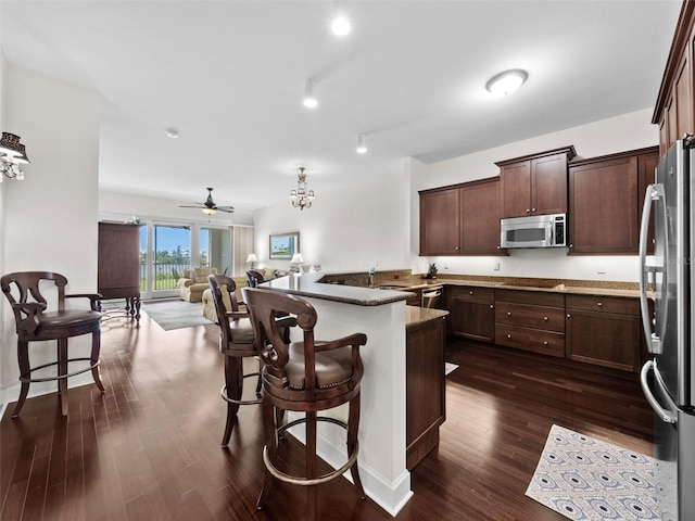 kitchen featuring appliances with stainless steel finishes, stone countertops, dark hardwood / wood-style flooring, a kitchen breakfast bar, and ceiling fan