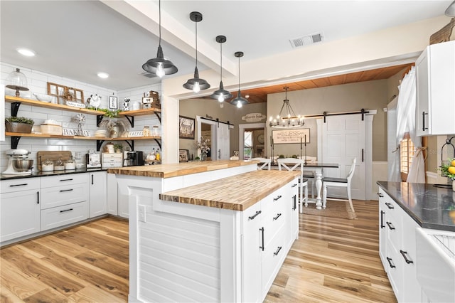 kitchen with hanging light fixtures, a barn door, light hardwood / wood-style flooring, and wood counters