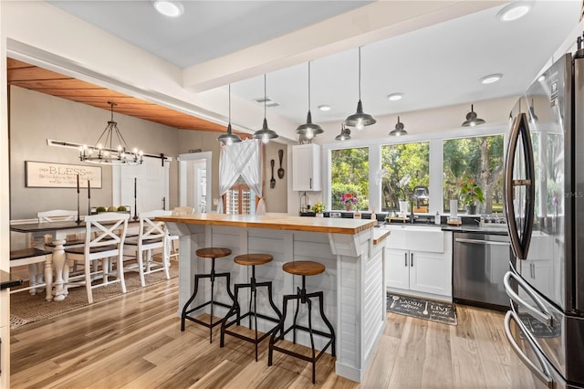 kitchen with white cabinets, appliances with stainless steel finishes, light wood-type flooring, and pendant lighting