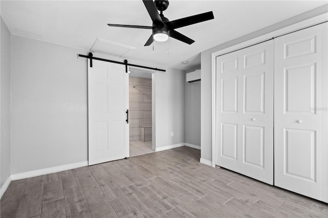 unfurnished bedroom featuring ceiling fan, a closet, ensuite bath, an AC wall unit, and a barn door