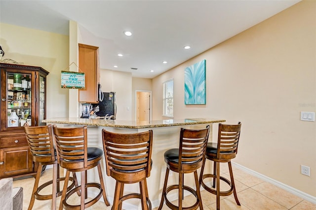 kitchen with kitchen peninsula, backsplash, a breakfast bar area, light stone counters, and light tile floors