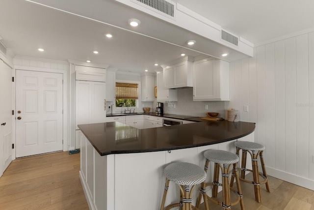 kitchen featuring white cabinetry, a kitchen breakfast bar, light hardwood / wood-style floors, and tasteful backsplash