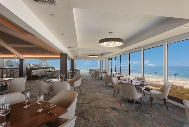 interior space with a view of the beach, a raised ceiling, and a water view