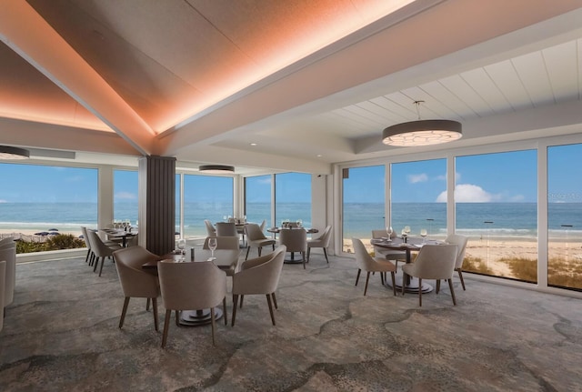 dining space featuring a view of the beach, a water view, and a raised ceiling