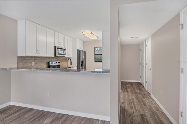 kitchen with light stone countertops, stainless steel appliances, white cabinets, and dark wood-type flooring