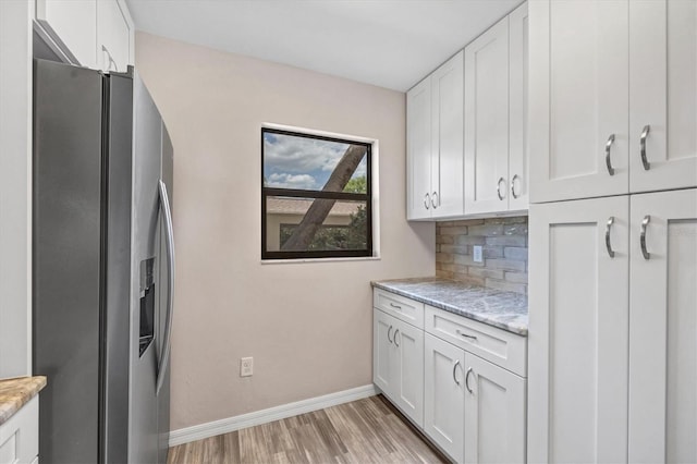 kitchen featuring stainless steel fridge, light hardwood / wood-style flooring, white cabinets, light stone counters, and tasteful backsplash