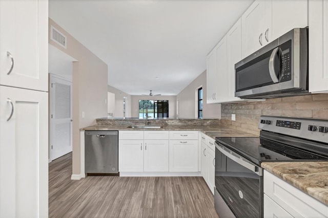 kitchen with light hardwood / wood-style floors, appliances with stainless steel finishes, white cabinets, kitchen peninsula, and sink