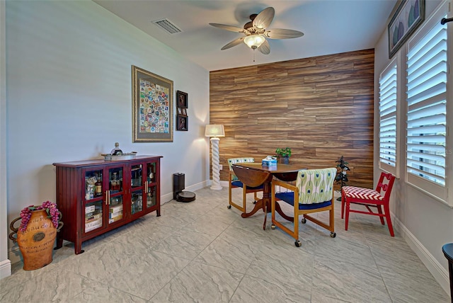 dining area featuring wood walls, ceiling fan, and light tile flooring