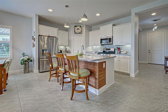 kitchen featuring appliances with stainless steel finishes, hanging light fixtures, white cabinets, and a center island with sink