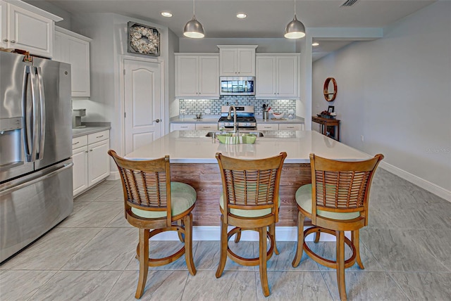 kitchen with tasteful backsplash, stainless steel appliances, a center island with sink, and hanging light fixtures