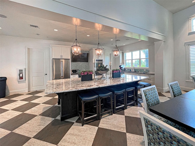 kitchen with hanging light fixtures, stainless steel fridge, white cabinetry, and a breakfast bar area