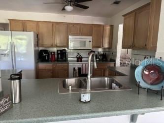 kitchen featuring white appliances, a breakfast bar area, kitchen peninsula, ceiling fan, and sink