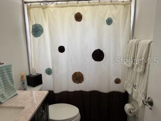 bathroom featuring toilet, a shower with shower curtain, and vanity