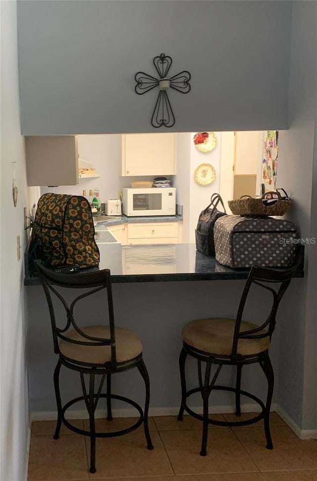 kitchen with white microwave, tile patterned flooring, a kitchen bar, and white cabinets