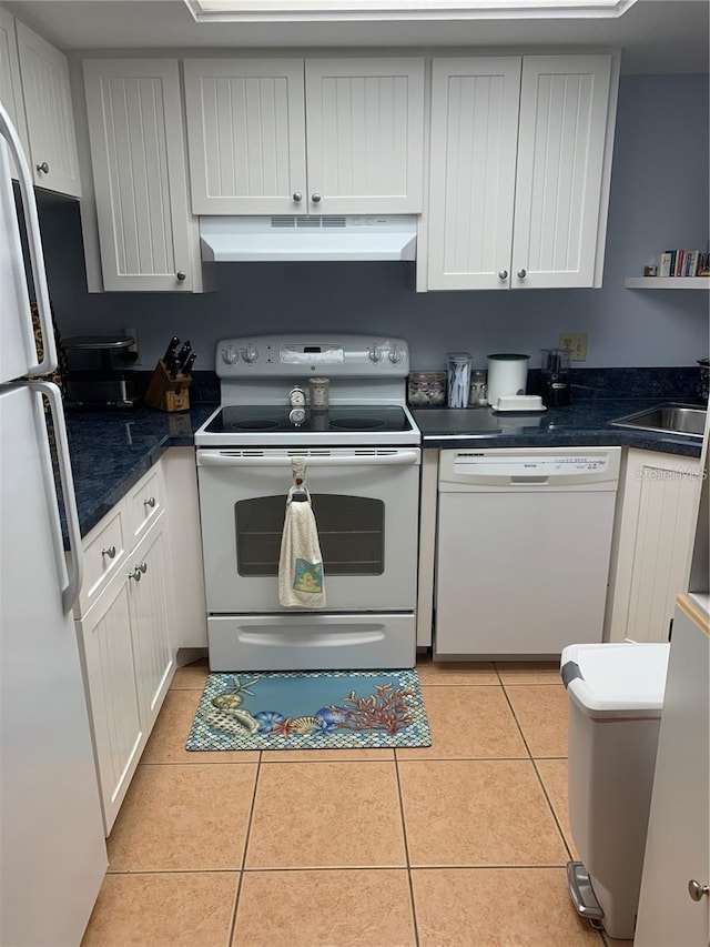 kitchen with light tile patterned floors, white appliances, dark countertops, and under cabinet range hood