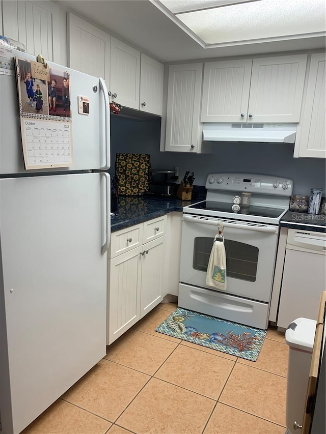 kitchen featuring light tile patterned floors, white appliances, dark countertops, and under cabinet range hood