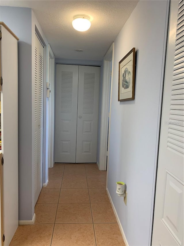 hall with a textured ceiling, light tile patterned flooring, and baseboards