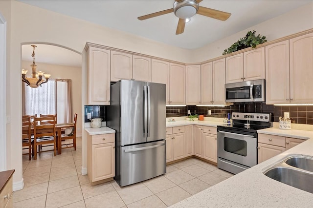 kitchen with backsplash, ceiling fan with notable chandelier, stainless steel appliances, and light tile floors