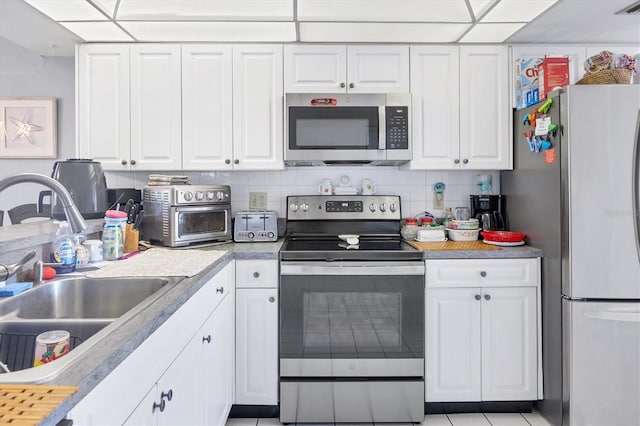 kitchen featuring appliances with stainless steel finishes, backsplash, light tile flooring, and white cabinets