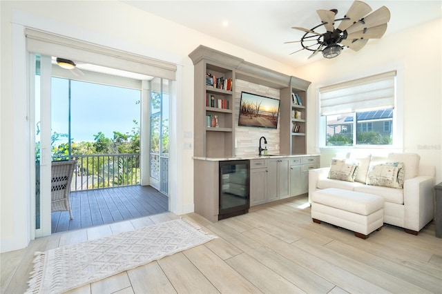 living area with ceiling fan, light hardwood / wood-style floors, beverage cooler, sink, and built in shelves