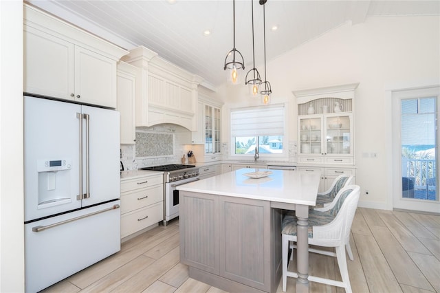 kitchen with decorative light fixtures, tasteful backsplash, high quality appliances, a center island, and light wood-type flooring