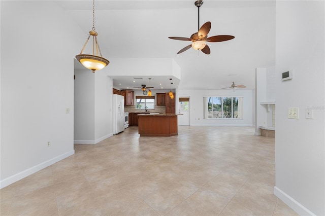 unfurnished living room featuring a towering ceiling, sink, ceiling fan, and light tile floors