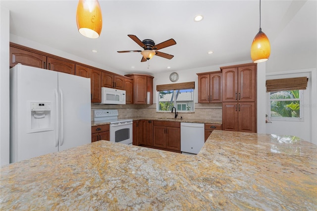 kitchen with light stone counters, white appliances, a sink, decorative backsplash, and pendant lighting