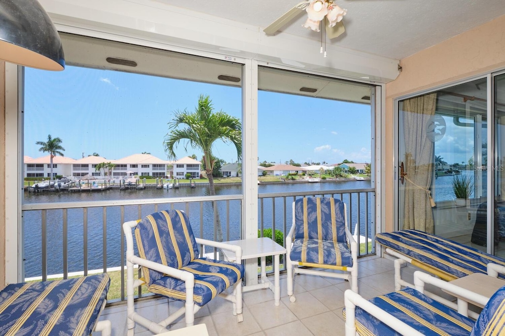 sunroom with ceiling fan and a water view