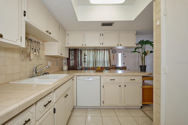 kitchen with backsplash, tile counters, dishwasher, white cabinets, and light tile floors